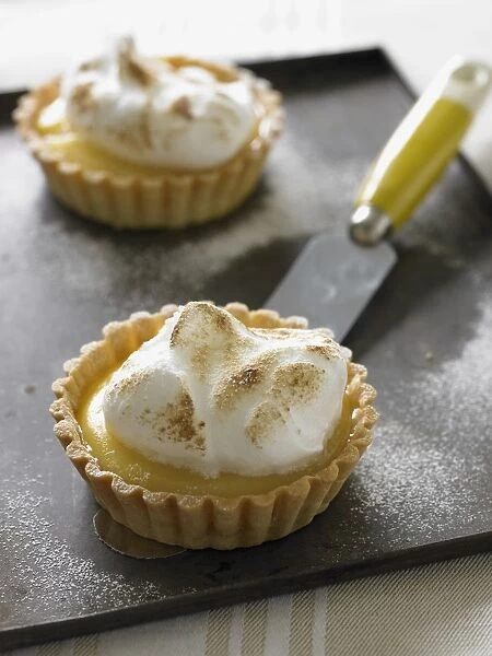 Lemon meringue tartlets on baking tray, with palette knife