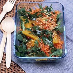 Moroccan rocket, carrot and orange salad with paprika dressing and sesame seeds, in glass dish, wooden cutlery nearby