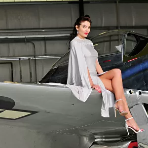 Elegant model in a silver gown sitting with legs crossed on the wing of a P-51 Mustang