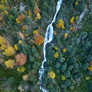 Aerial view of waterfall in the Urdiceto Ravine surrounded by mixed autumnal forest, Pyrenees Mountains, Aragon, Spain. November