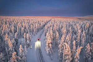 Finland Photo Mug Collection: Aerial view of car on icy road and illuminated headlamps driving in the snowcapped forest