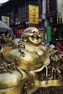 District Collection: A golden statue of a reclining laughing Buddha covered in small Buddhas