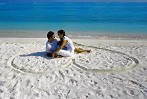 Related Images Framed Print Collection: Young couple on beach sitting in a heart shaped imprint on the sand, Maldives