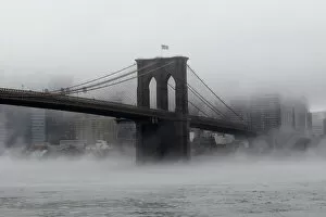 Related Images Photo Mug Collection: The Brooklyn Bridge is seen partially in fog from in front of the Manhattan skyline