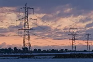 Power Line Collection: Electricity transmission pylons and overhead wires, crossing over snow covered farmland at sunset