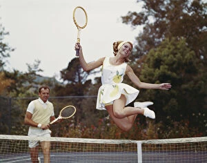 Mid Adult Men Collection: Couple on tennis court, woman jumping in foreground
