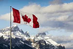 Typically Canadian Collection: Canadian Flag Blowing In The Wind On A Flag Pole With Snow Covered Mountain Range In The
