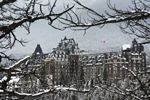 Typically Canadian Collection: Snow Covered Banff Springs Hotel Framed By Tree Limbs With Snow Covered Trees On Mountain Hillside