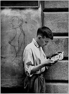 Street art graffiti Canvas Print Collection: Boy intent on reading a comic strip in the street